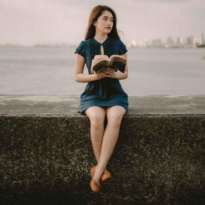 selective focus photography of sitting woman holding open book